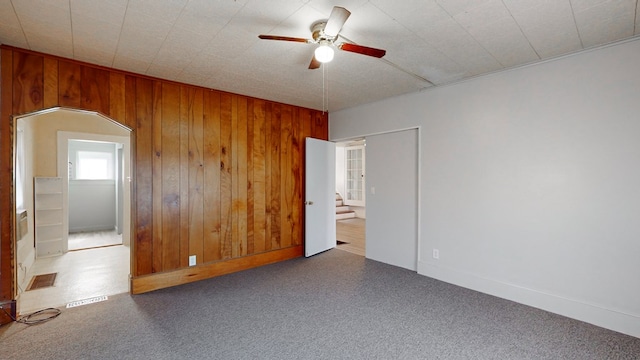 carpeted empty room with ceiling fan and wooden walls