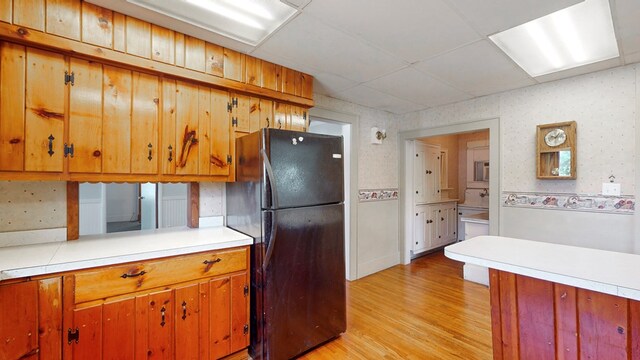 kitchen featuring black refrigerator, light hardwood / wood-style flooring, and a drop ceiling