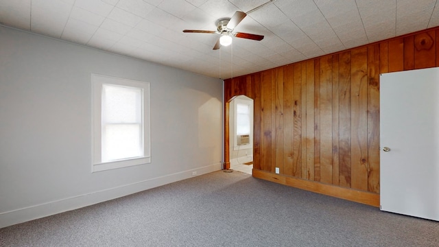 spare room featuring carpet floors, wooden walls, and ceiling fan