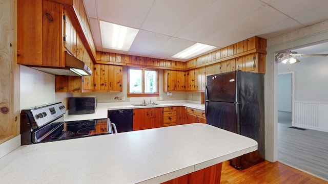 kitchen featuring black appliances, light wood-type flooring, kitchen peninsula, ceiling fan, and a drop ceiling