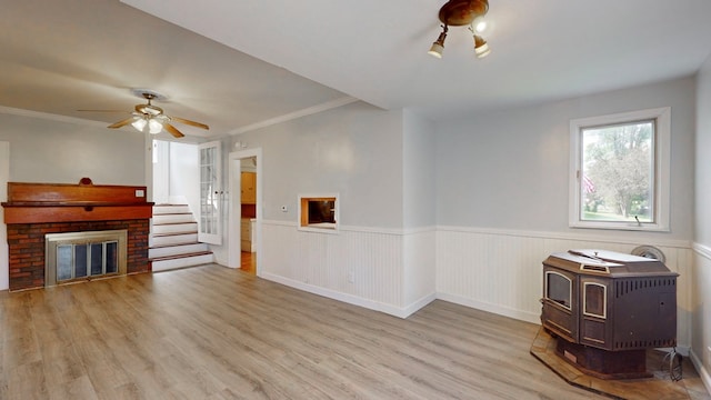 unfurnished living room with ceiling fan, a brick fireplace, crown molding, and light wood-type flooring