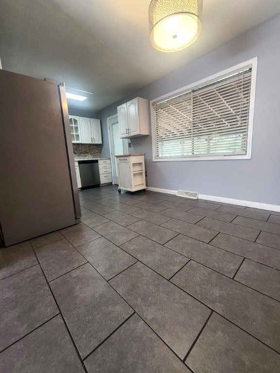 kitchen with stainless steel appliances, dark tile patterned floors, decorative backsplash, and white cabinets