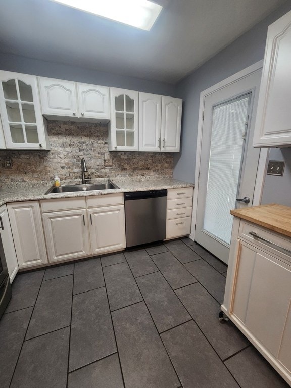 kitchen featuring sink, white cabinetry, stainless steel dishwasher, dark tile patterned flooring, and backsplash