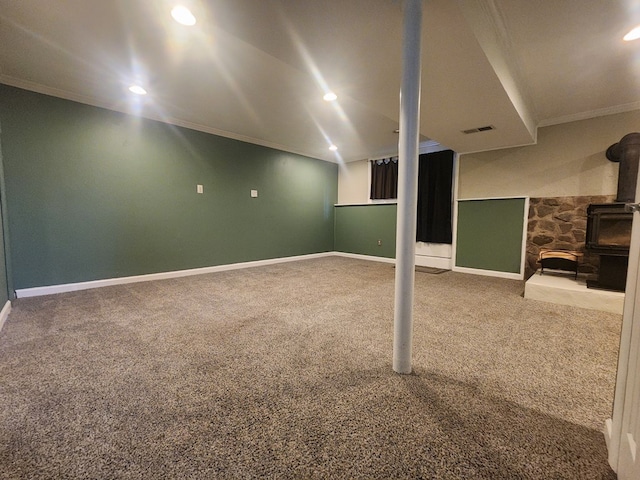 basement with carpet flooring, ornamental molding, and a wood stove