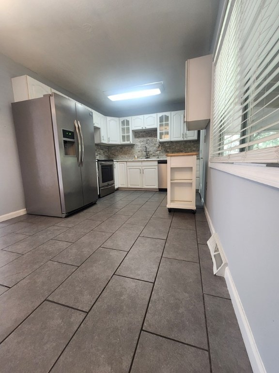 kitchen with white cabinetry, sink, backsplash, dark tile patterned floors, and stainless steel appliances