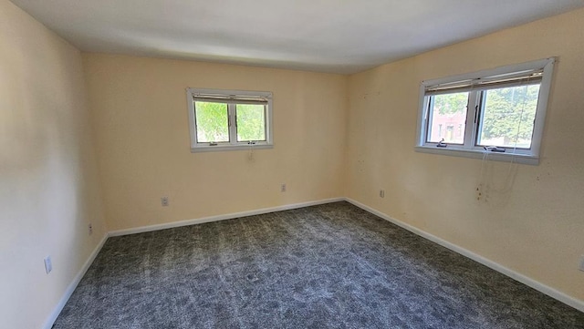 empty room featuring a healthy amount of sunlight and dark colored carpet