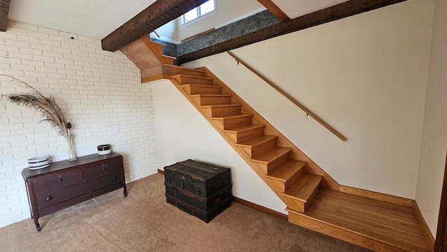 stairway featuring beamed ceiling, brick wall, and carpet