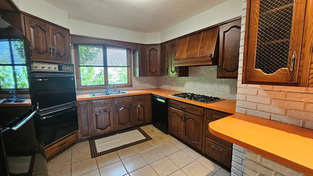 kitchen featuring dark brown cabinetry, sink, light tile patterned floors, decorative backsplash, and black appliances