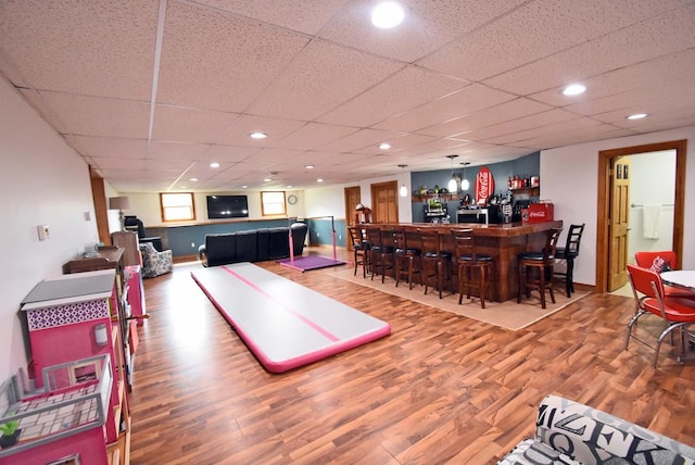 recreation room with wood-type flooring, a paneled ceiling, and indoor bar