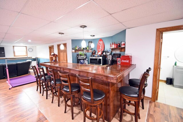 bar featuring decorative light fixtures, light hardwood / wood-style flooring, and a drop ceiling