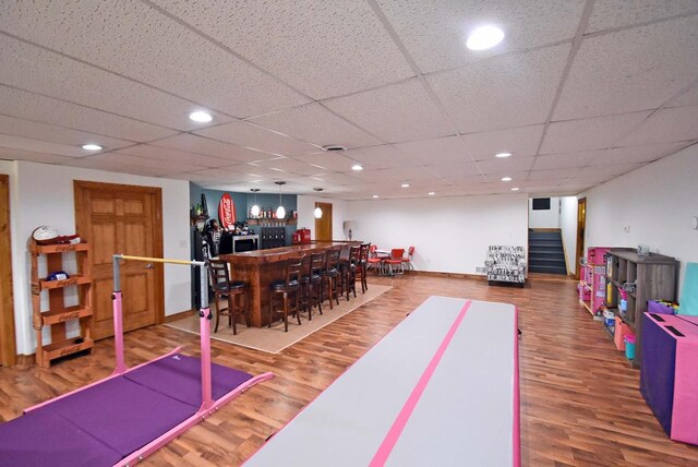 playroom featuring hardwood / wood-style flooring, a paneled ceiling, and bar area