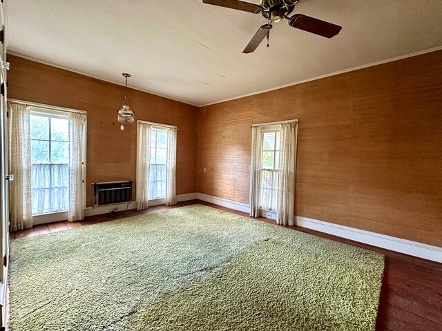 unfurnished living room featuring heating unit, ceiling fan, plenty of natural light, and wood-type flooring