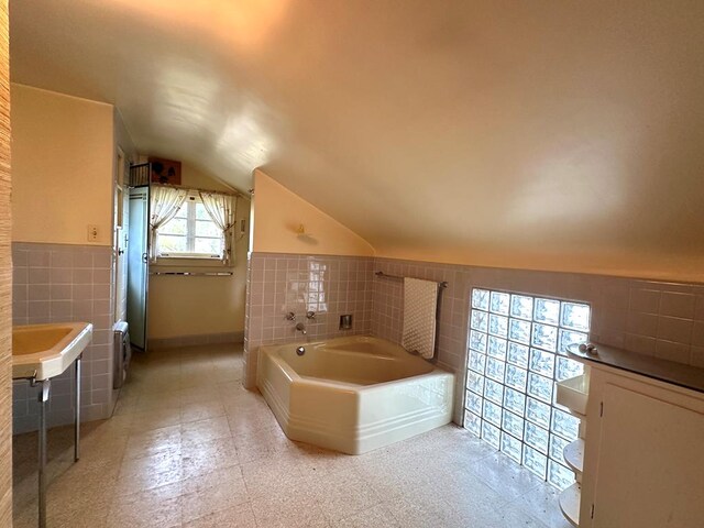 bathroom with a bathing tub, lofted ceiling, and tile walls