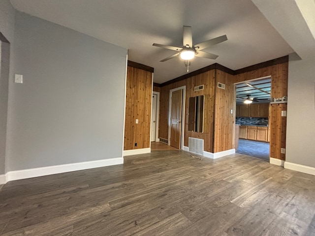 unfurnished living room featuring crown molding, wooden walls, dark hardwood / wood-style floors, and ceiling fan