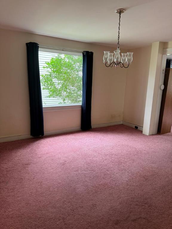 empty room featuring a chandelier and carpet floors