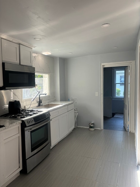 kitchen featuring backsplash, stainless steel range with gas stovetop, sink, and white cabinets