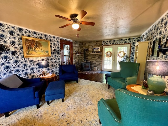 living room featuring french doors, a wood stove, hardwood / wood-style flooring, ceiling fan, and a textured ceiling