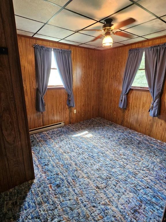 carpeted empty room featuring baseboard heating, ceiling fan, and wooden walls