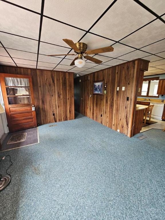 interior space featuring wooden walls, a paneled ceiling, ceiling fan, and carpet