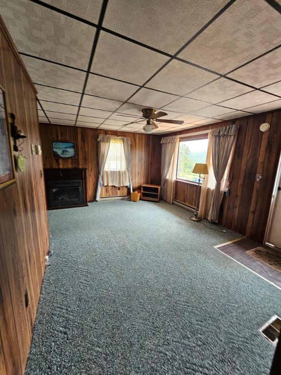 interior space with ceiling fan, wooden walls, carpet flooring, and a drop ceiling