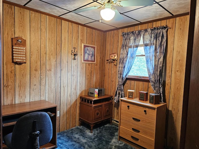 office area featuring wooden walls, ceiling fan, and dark colored carpet