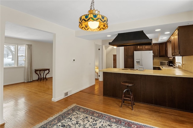 kitchen featuring sink, white refrigerator with ice dispenser, island exhaust hood, kitchen peninsula, and light wood-type flooring