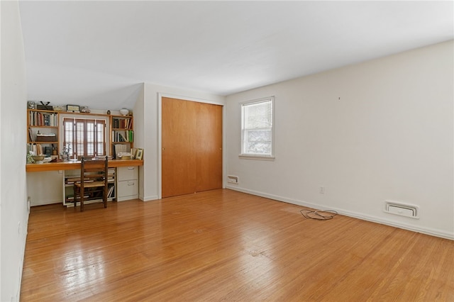 unfurnished room with built in desk, light hardwood / wood-style flooring, and a healthy amount of sunlight