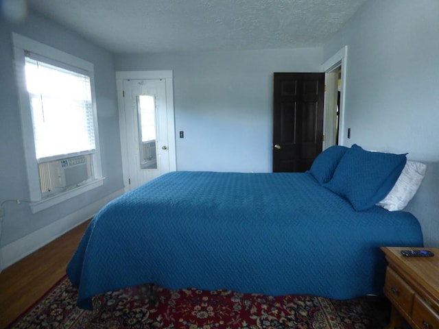 bedroom featuring dark wood-type flooring, cooling unit, and a textured ceiling