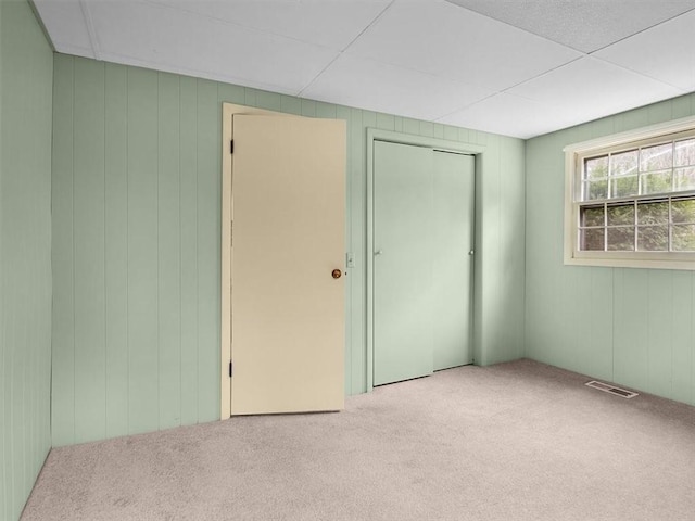 unfurnished bedroom with light colored carpet, a closet, and wood walls