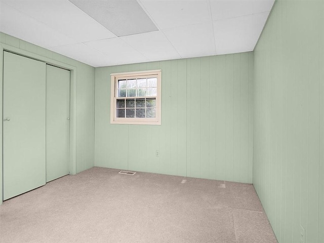 unfurnished bedroom with light colored carpet, wood walls, and a closet