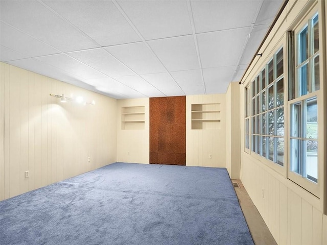 spare room featuring built in features, wood walls, and carpet flooring