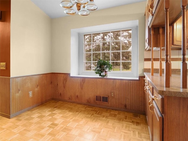 unfurnished room with an inviting chandelier, wood walls, light parquet flooring, and a wealth of natural light