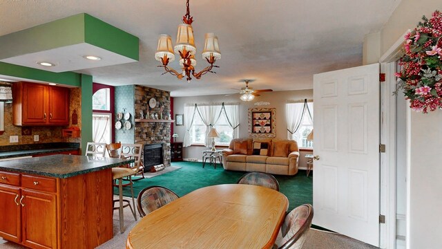 dining space featuring carpet, ceiling fan with notable chandelier, a textured ceiling, and a fireplace