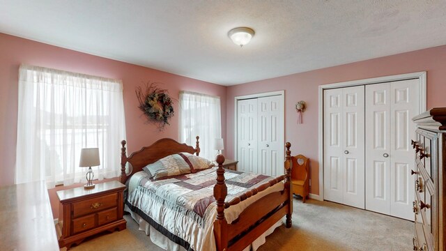 bedroom featuring multiple closets, light carpet, multiple windows, and a textured ceiling