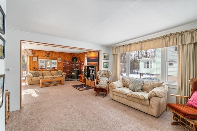 living room with carpet flooring, ornamental molding, wooden walls, and a wood stove