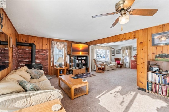 carpeted living room with a healthy amount of sunlight, a wood stove, and wooden walls