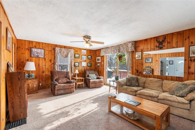 carpeted living room featuring ceiling fan, a textured ceiling, and wood walls