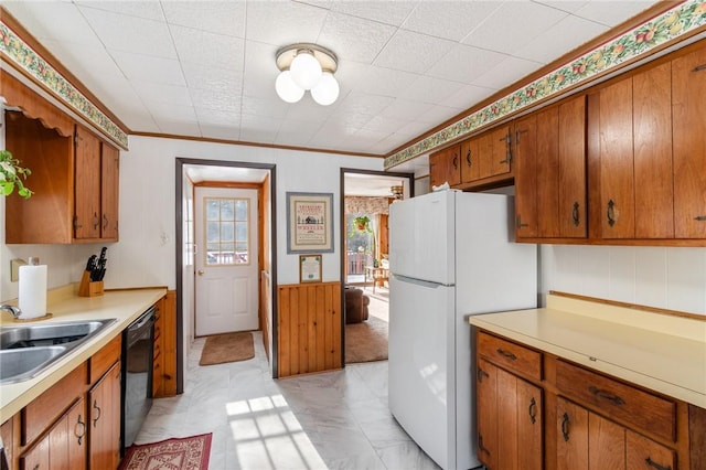 kitchen featuring sink, white fridge, black dishwasher, ornamental molding, and wood walls