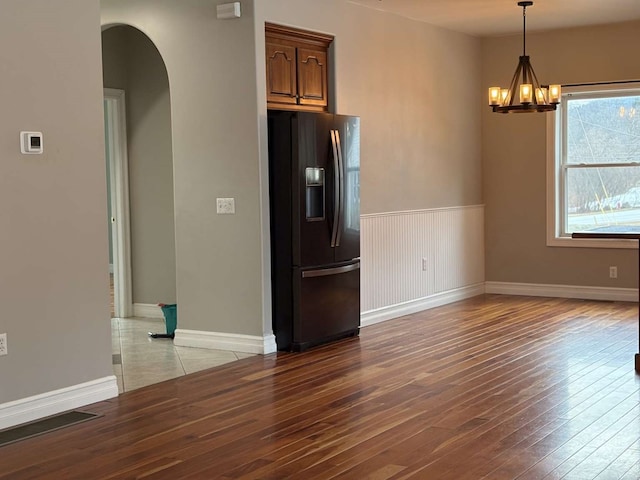 interior space with hardwood / wood-style flooring, an inviting chandelier, black fridge with ice dispenser, and decorative light fixtures