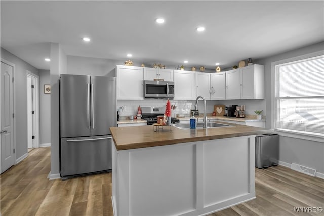 kitchen featuring sink, butcher block counters, stainless steel appliances, white cabinets, and a center island with sink