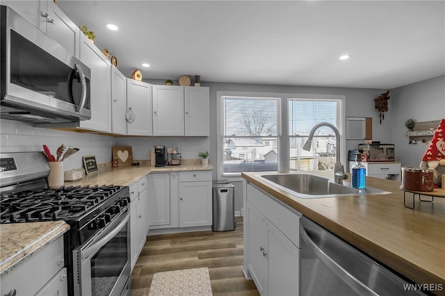 kitchen with appliances with stainless steel finishes, dark hardwood / wood-style floors, tasteful backsplash, white cabinetry, and sink