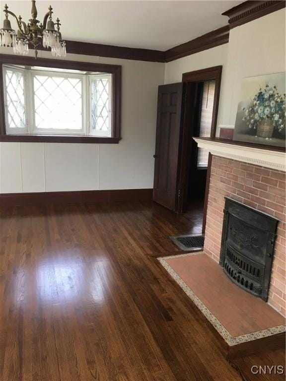 unfurnished living room with dark wood-type flooring, ornamental molding, a chandelier, and a brick fireplace