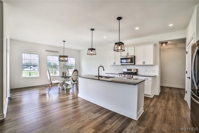 kitchen featuring appliances with stainless steel finishes, white cabinetry, a center island with sink, dark hardwood / wood-style flooring, and decorative light fixtures