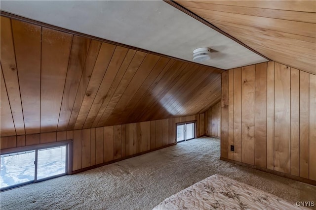 additional living space featuring a healthy amount of sunlight, wooden walls, vaulted ceiling, and light carpet