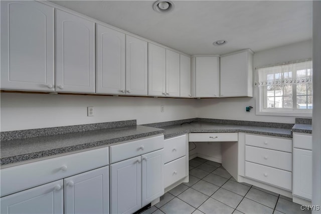 kitchen with white cabinetry, light tile patterned floors, and built in desk