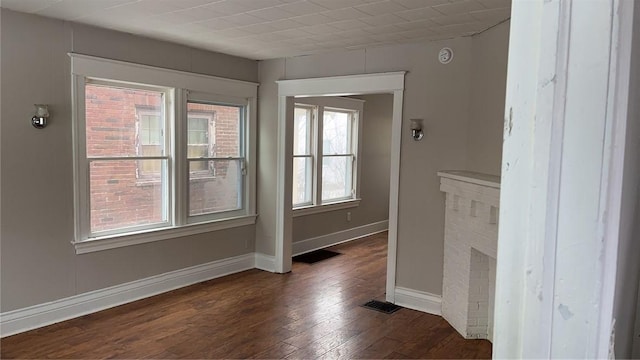 empty room with baseboards, visible vents, a fireplace, and dark wood finished floors