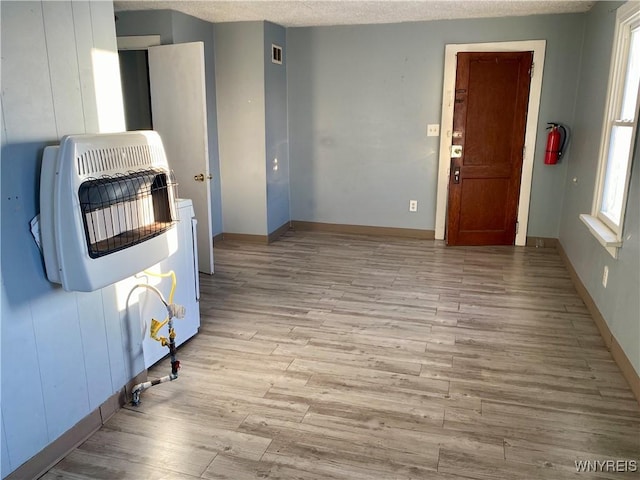 interior space featuring heating unit, a textured ceiling, and light wood-type flooring