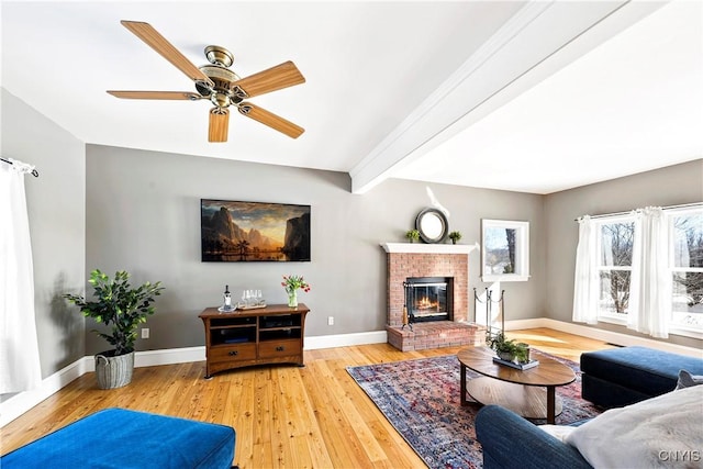 living room with a fireplace, light hardwood / wood-style flooring, beamed ceiling, and ceiling fan