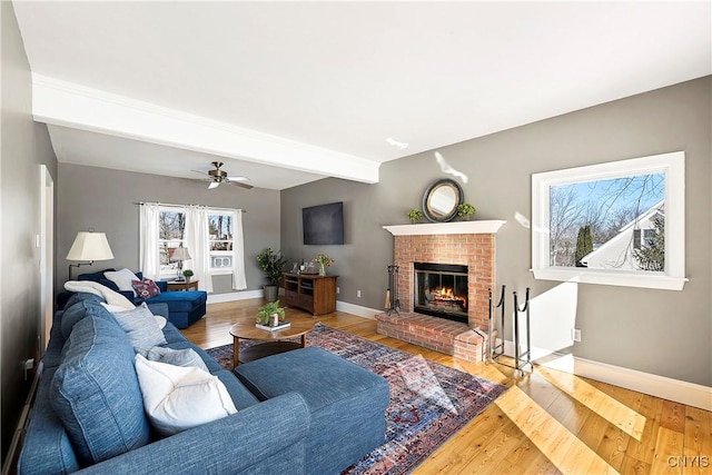 living room with hardwood / wood-style flooring, ceiling fan, a brick fireplace, and beam ceiling