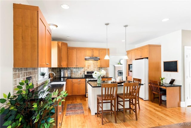 kitchen with a kitchen island, decorative light fixtures, a breakfast bar area, white refrigerator, and stainless steel gas range